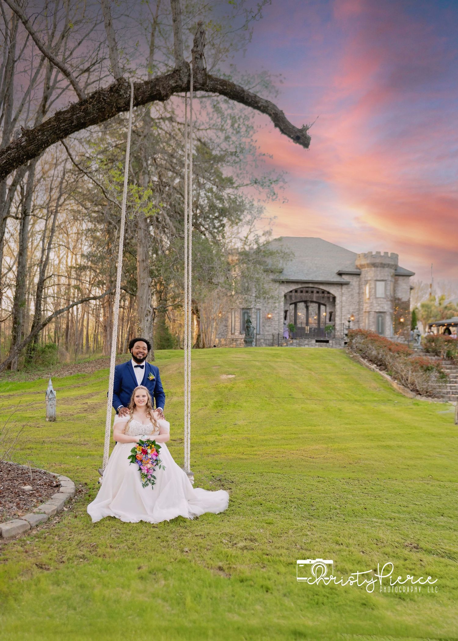 Scenic wedding photoshoot at sunset on a lush green lawn with elegant buildings and trees in the background.