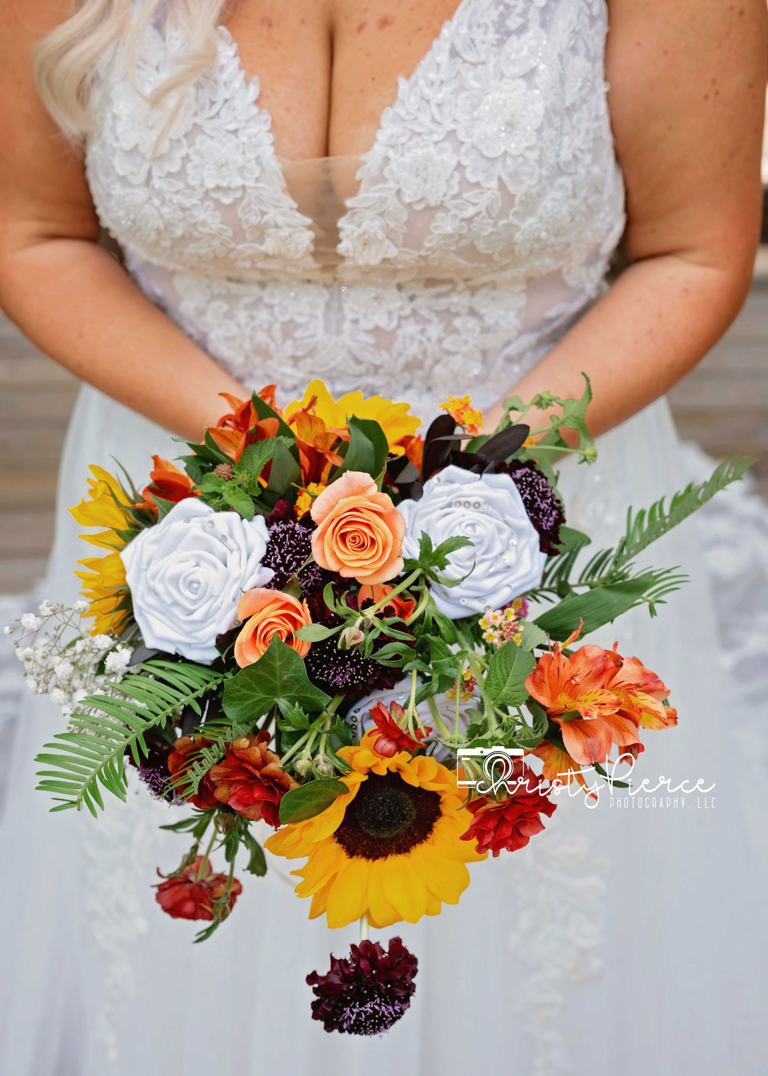 A row of colorful fall wedding bouquets featuring sunflowers, roses, and burgundy blooms held against white dresses.
