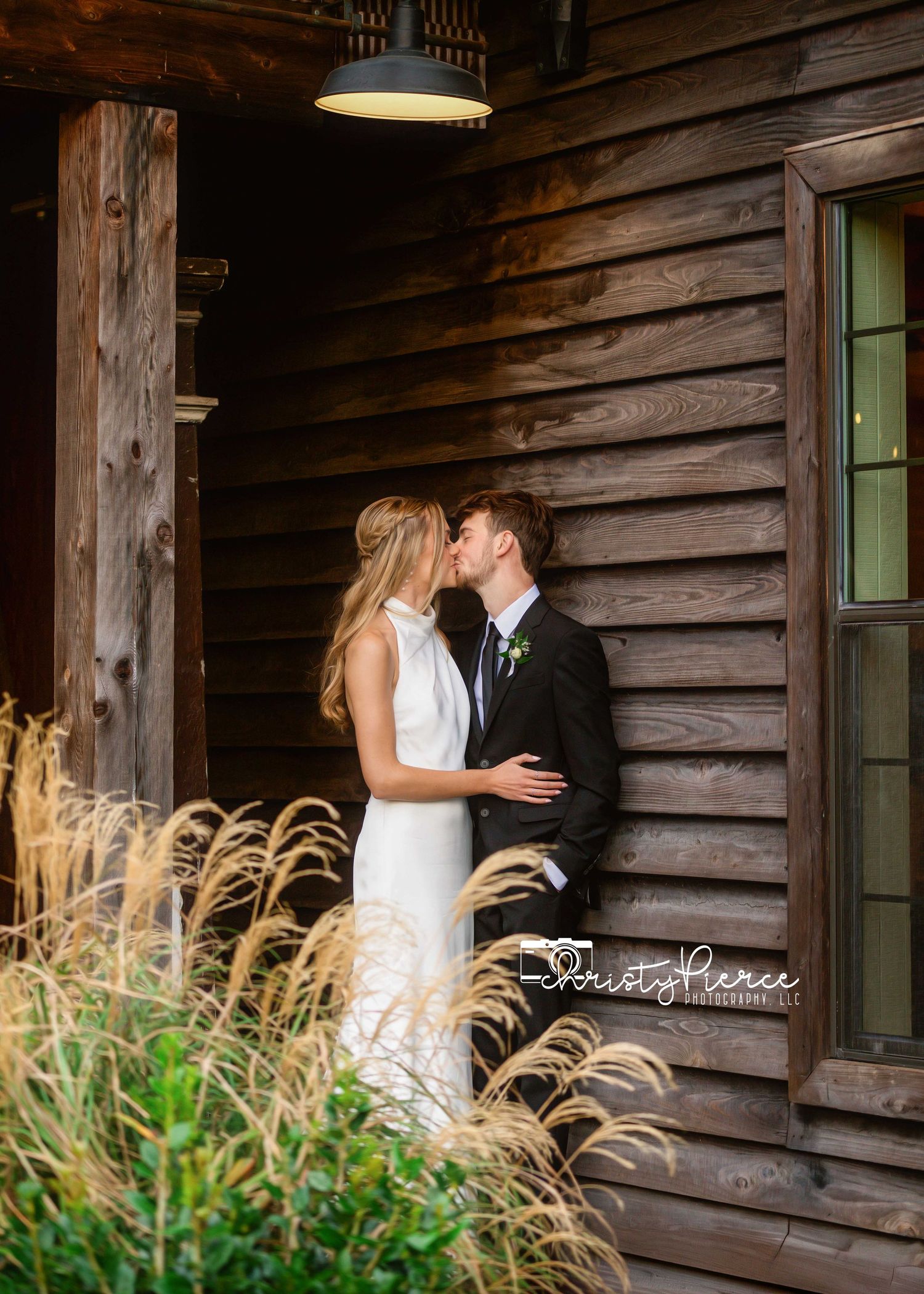 A romantic moment captured in front of a rustic log cabin wall with tall wheat grass swaying in the foreground.
