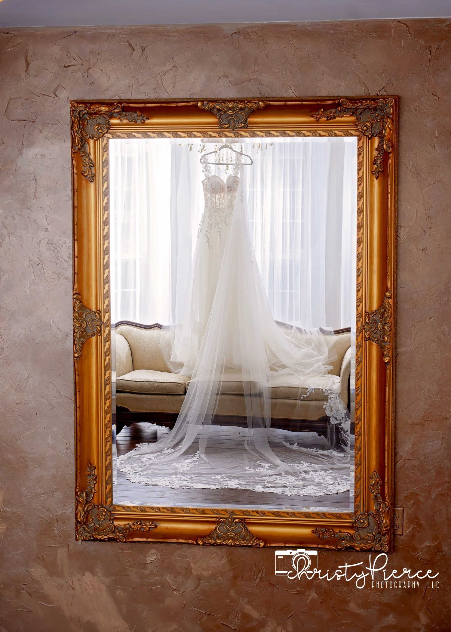 Elegant wedding dress reflected in ornate gold mirror, with flowing veil, captured by Christy Pierce Photography.