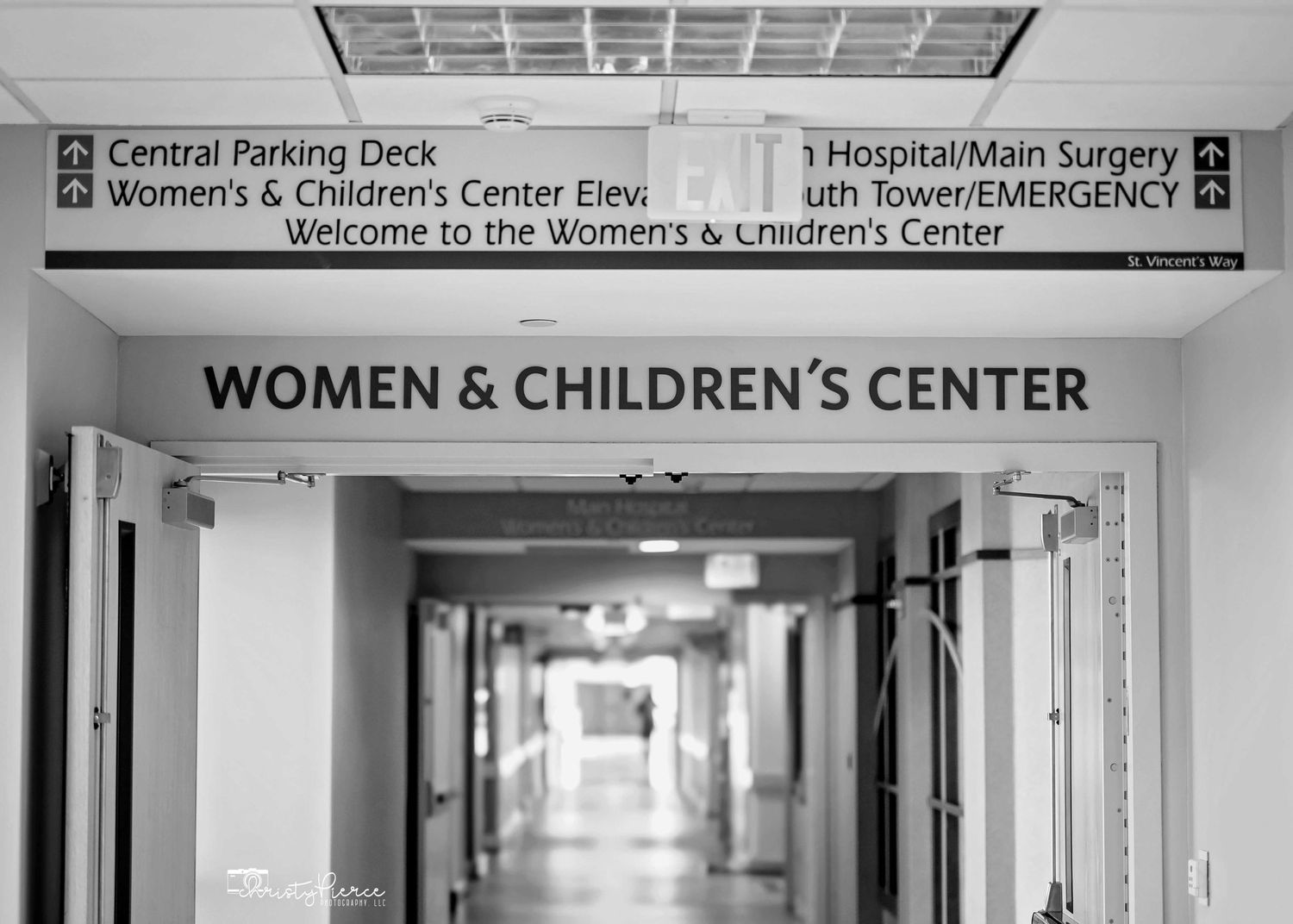 Black and white hospital hallway with sign for Women & Children's Center and directional signage above.