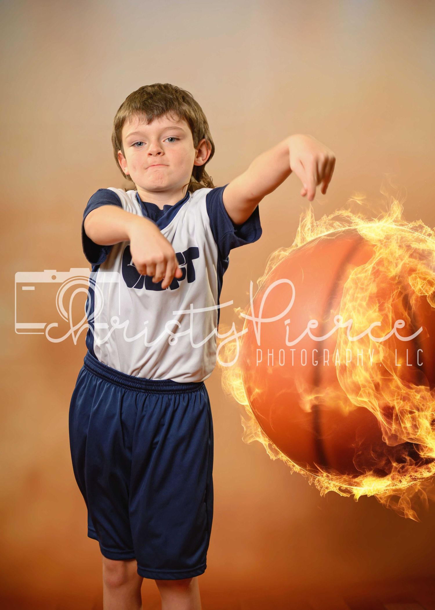 Young athlete in blue and white uniform performs basketball move beside a flaming basketball against brown background.