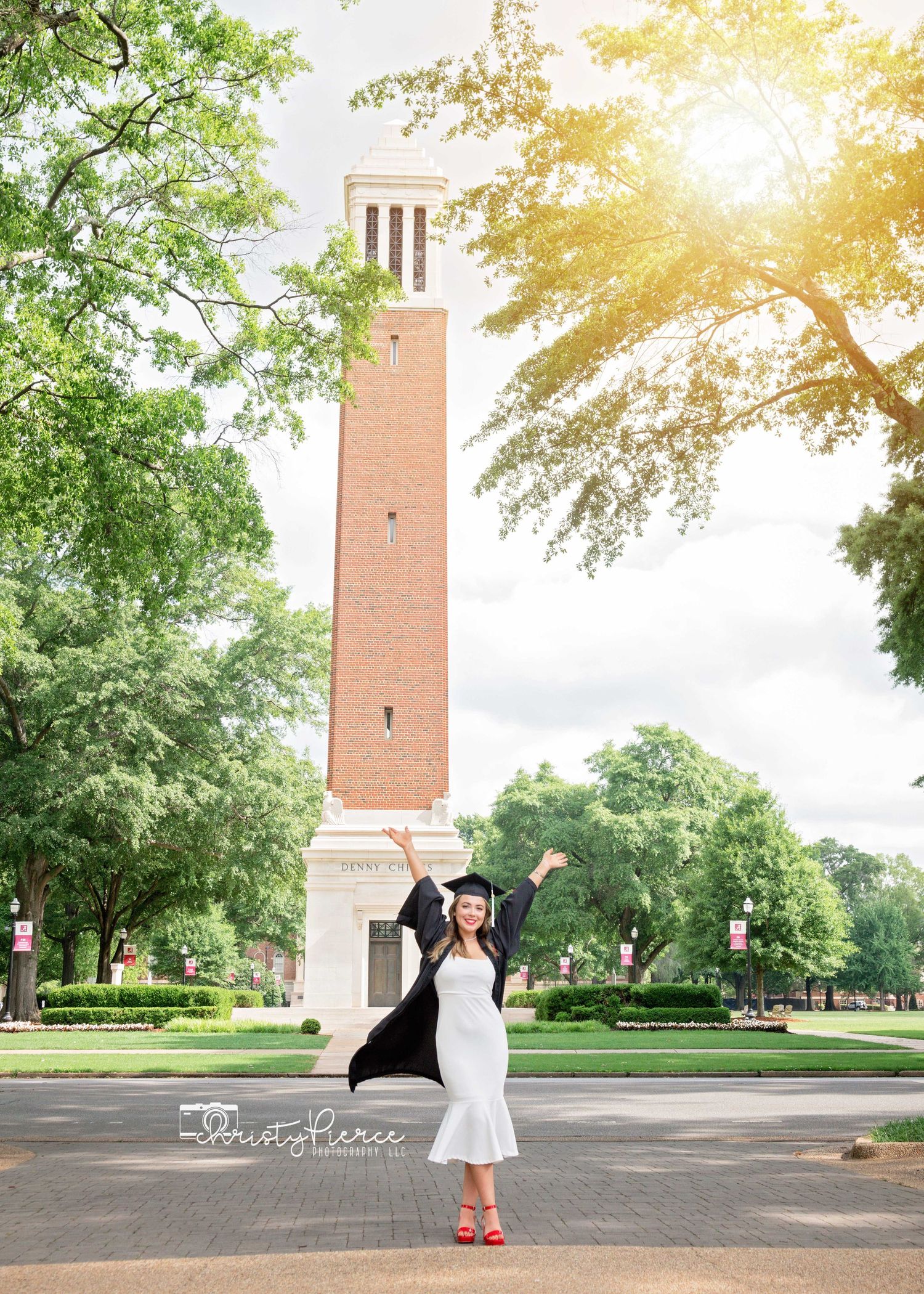 Graduation celebration photo on a college campus with Denny Chimes tower and green trees in warm sunset light.