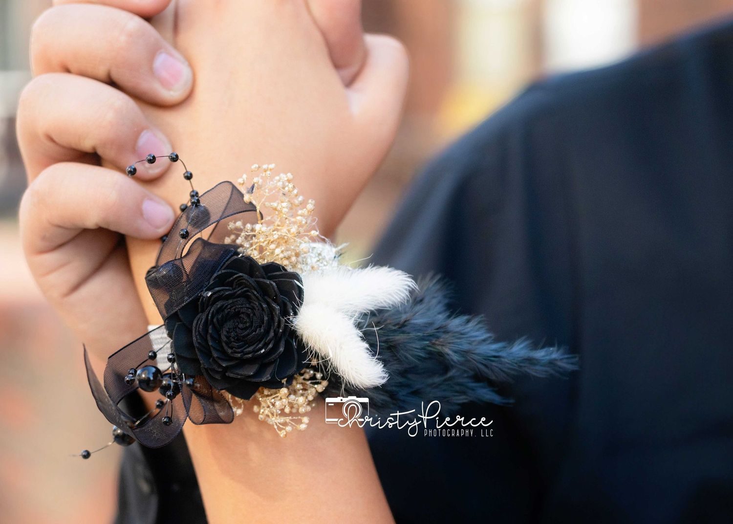 Black rose wrist corsage with feathers and beaded accents, elegant prom or formal event floral accessory.