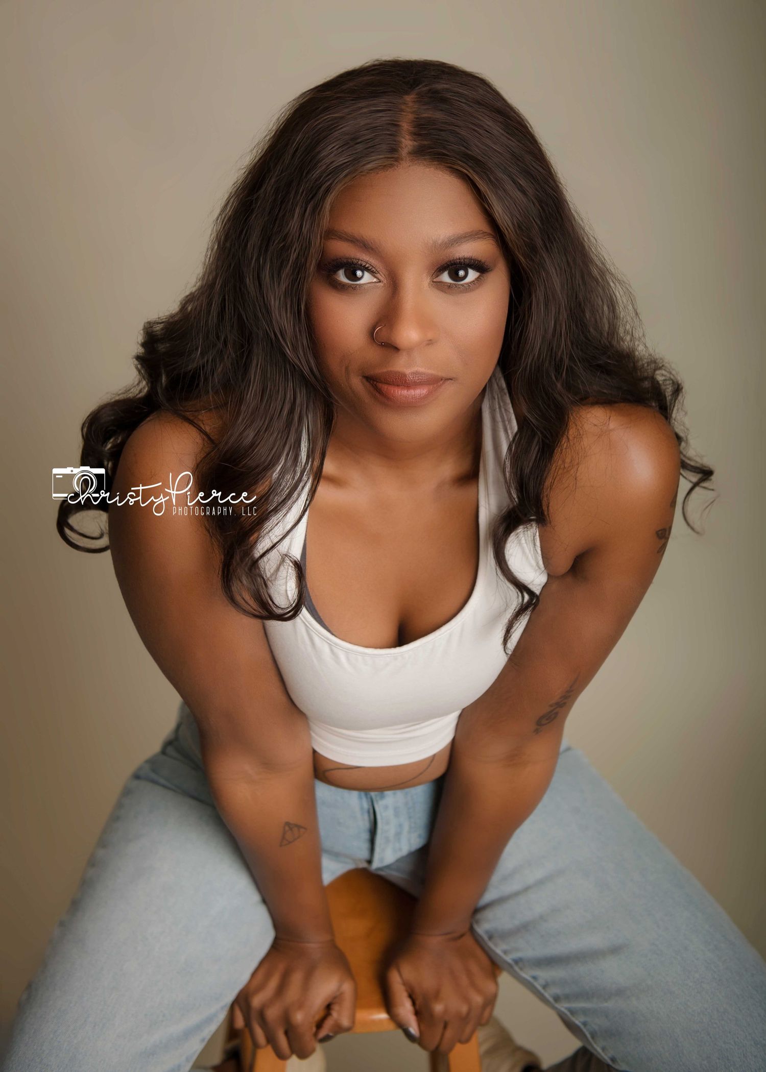 A portrait of someone in a white crop top and light jeans leaning forward in a studio setting with soft lighting.