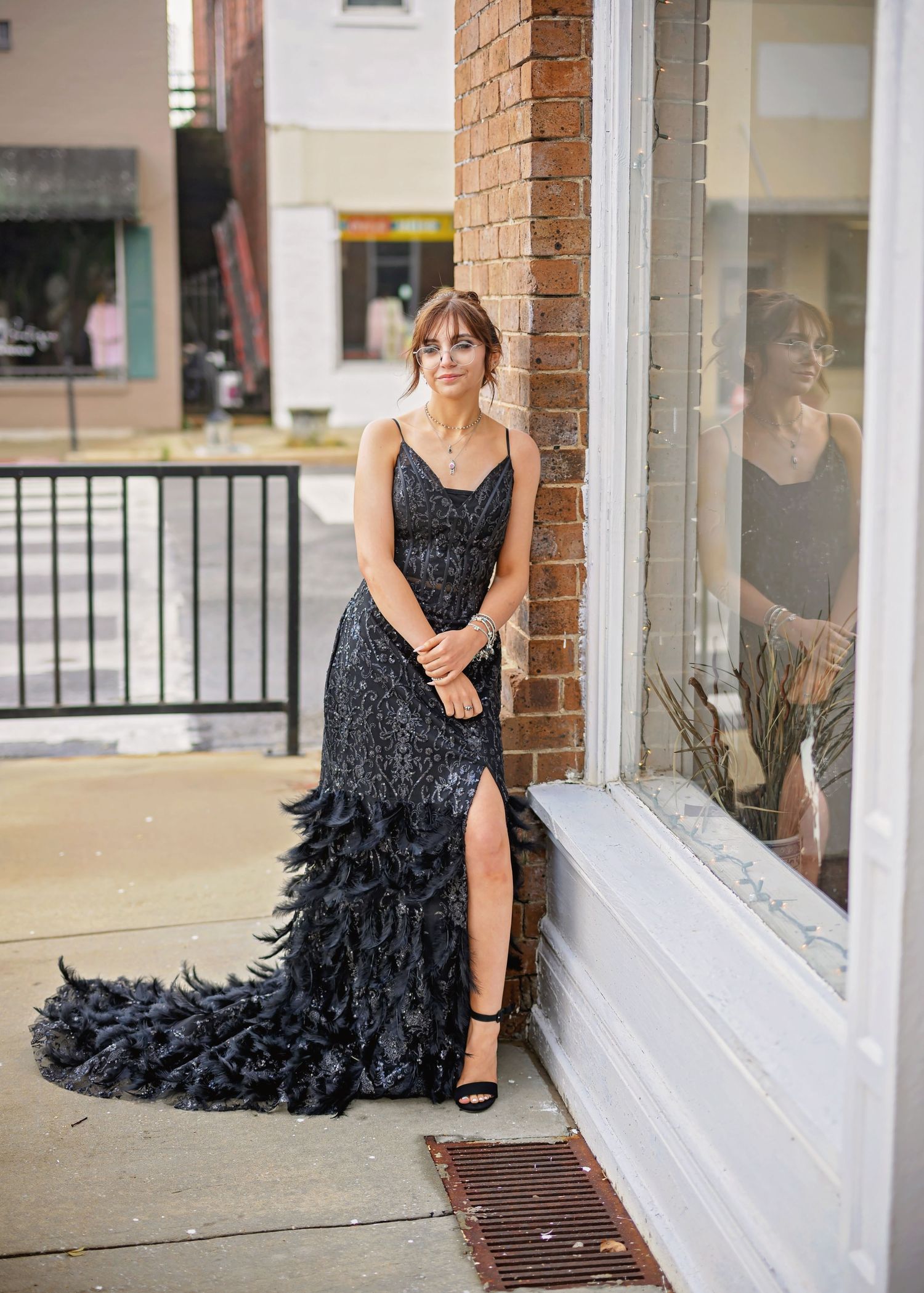 A woman in a black feathered evening gown poses elegantly on a porch with brick columns.