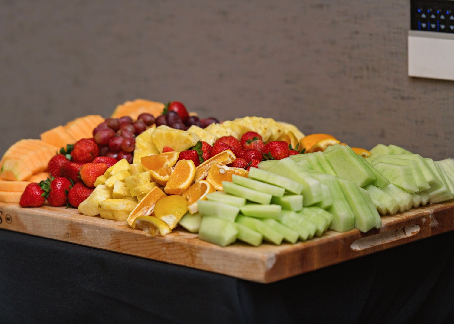 Fresh fruit platter with colorful assortment of melons, berries, and citrus slices arranged on wooden serving board.