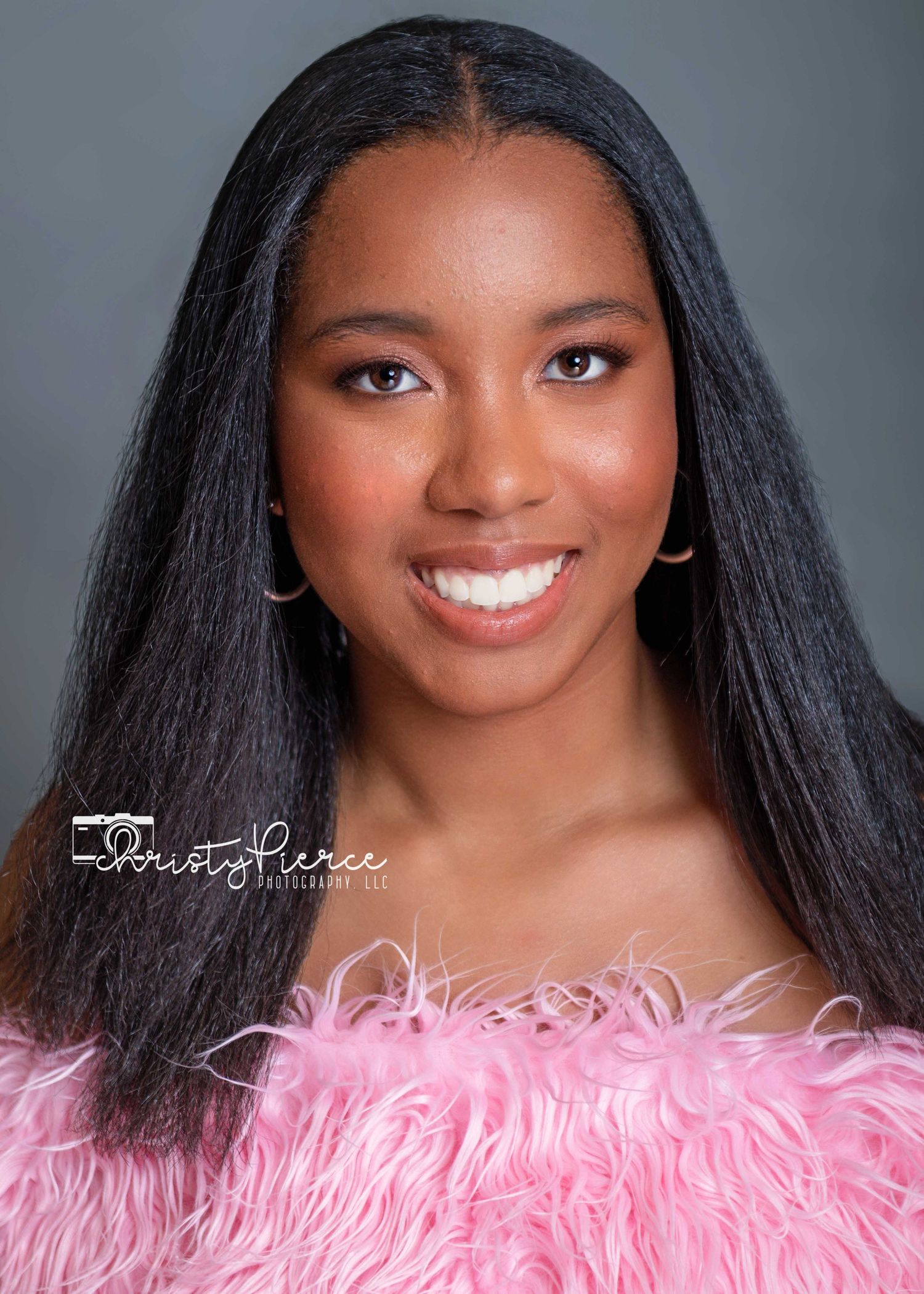 Portrait against gray background with pink feathered wrap and long dark hair.