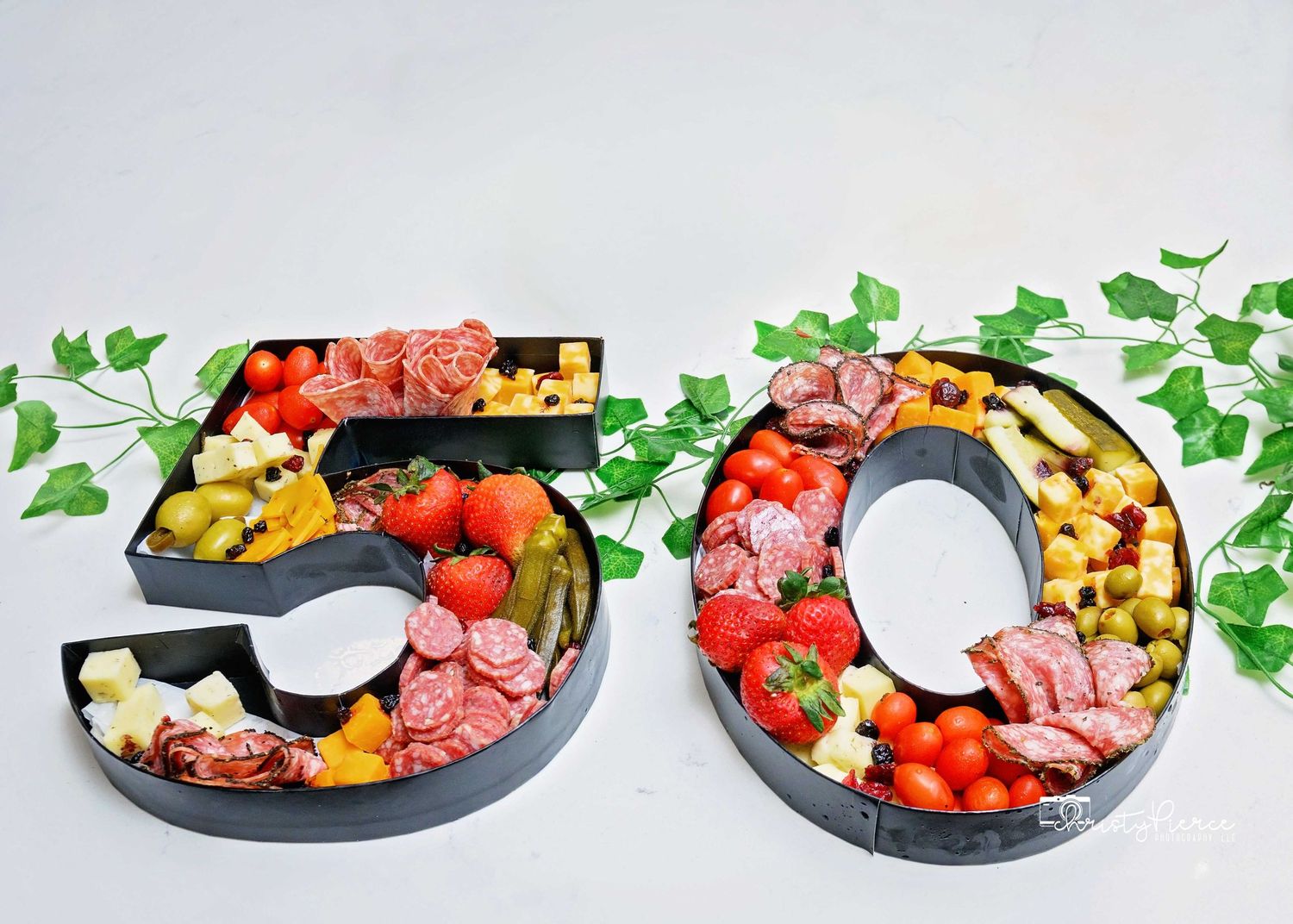 Number-shaped charcuterie boards filled with meats, cheeses, tomatoes and garnished with fresh herbs for a 50th celebration.