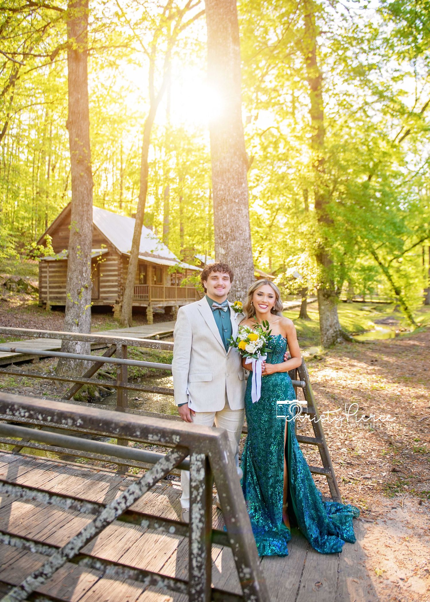 A rustic log cabin in the woods at sunset with a wooden bridge walkway in the foreground.