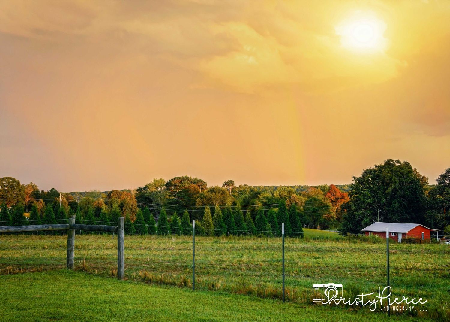 Golden sunset illuminates a pastoral farm landscape with a red barn and green pastures surrounded by trees.