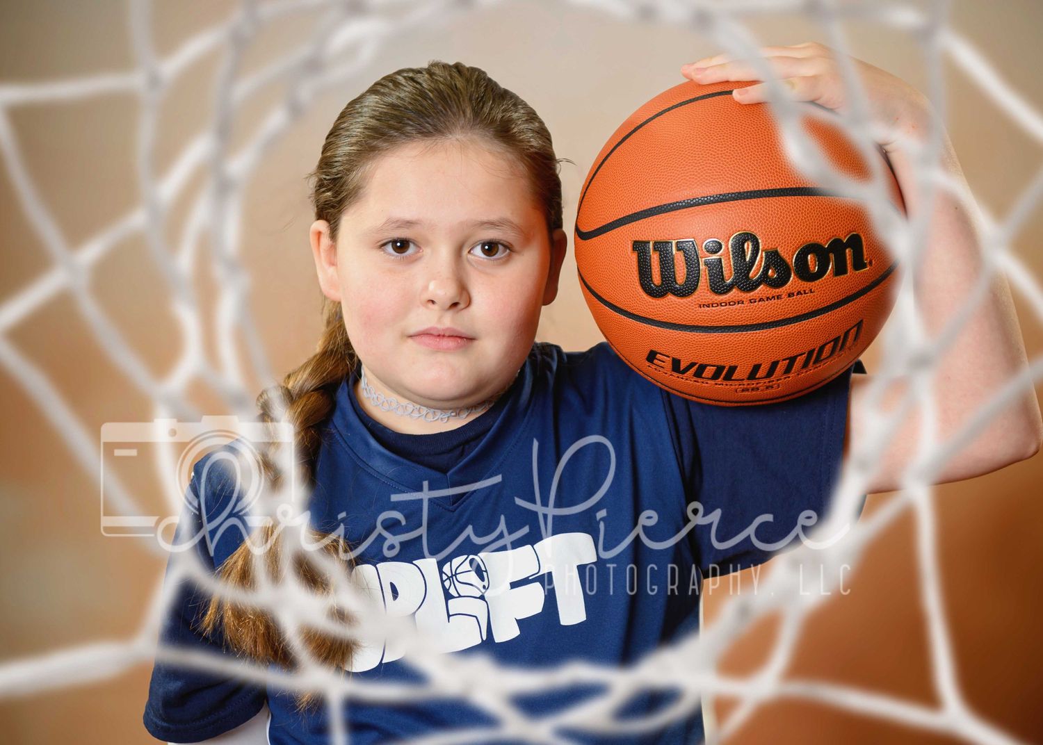 A basketball player in a navy blue jersey poses behind overlaid netting with a Wilson basketball.