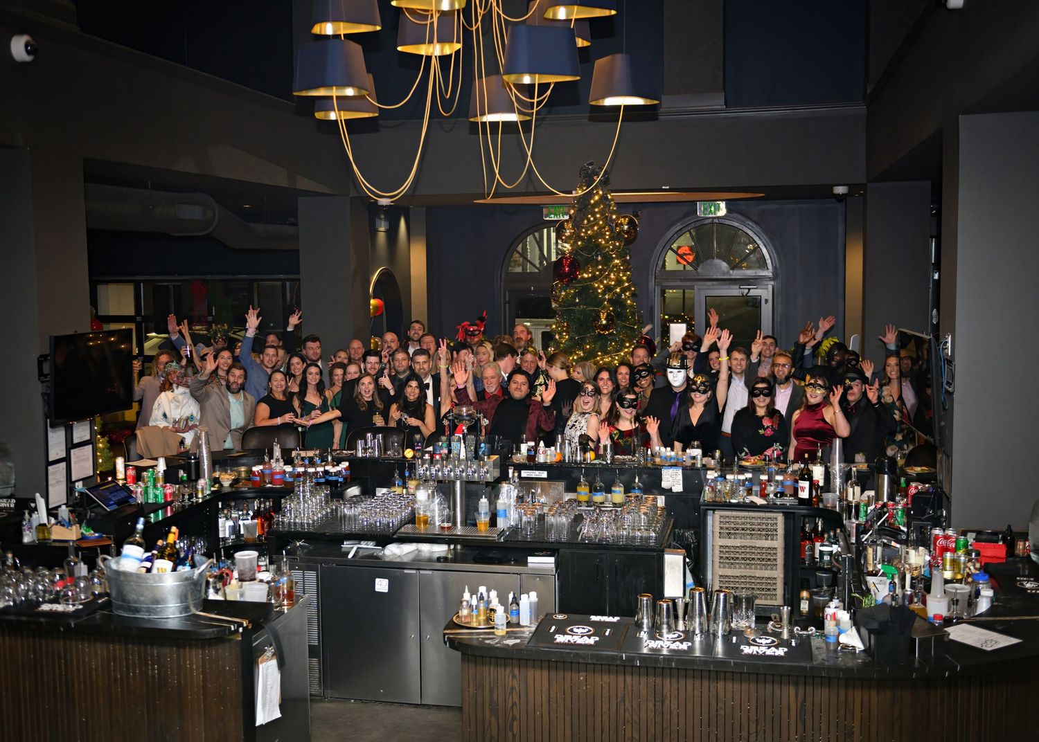 Large group of people seated at dining tables in an elegant restaurant with chandelier lighting and modern decor.