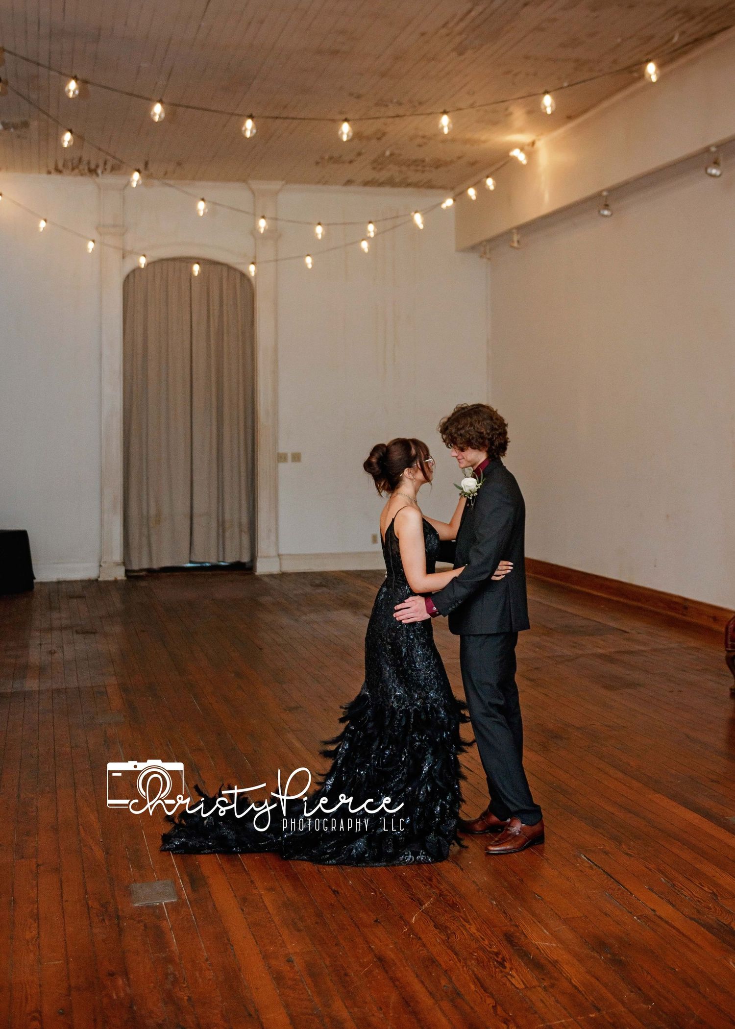 Romantic couple dancing in an elegant studio space with string lights and wooden floors creating an intimate atmosphere.