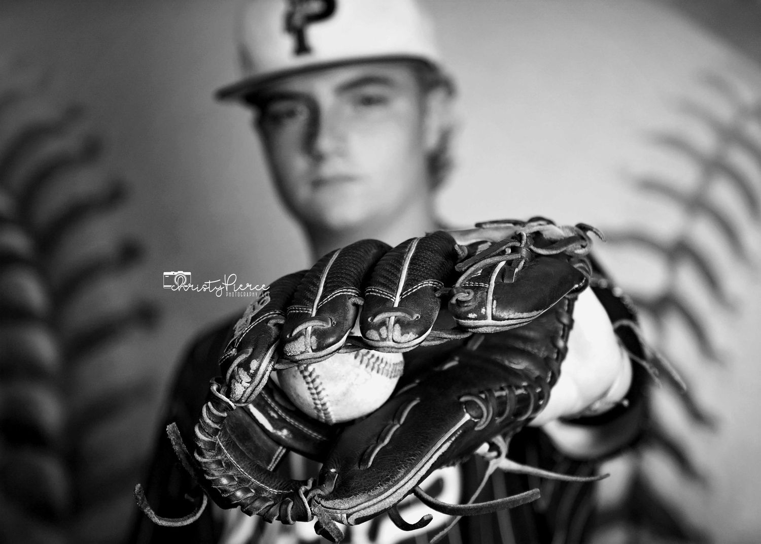 A black and white close-up photo of a baseball glove with a baseball showing detailed stitching and leather texture.