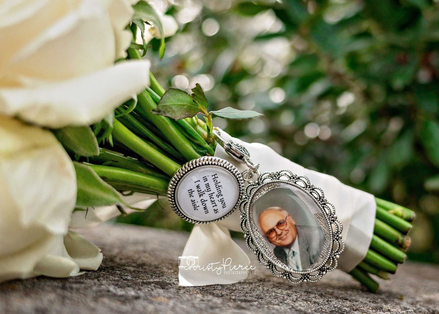 Wedding bouquet with white roses and a memorial charm featuring a photo and quote, honoring a loved one on a special day.