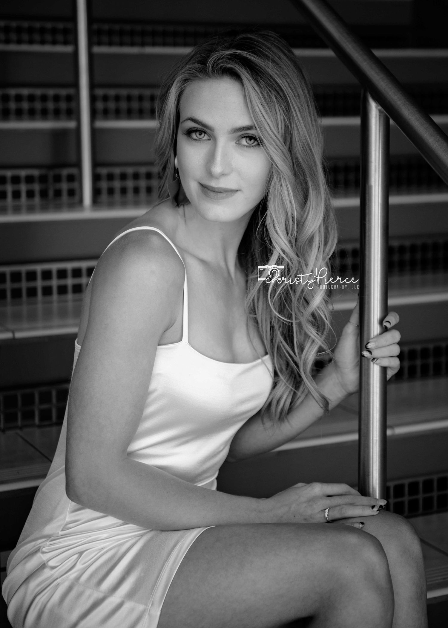 Black and white portrait of a blonde woman in a white dress sitting gracefully on stairs holding a railing.