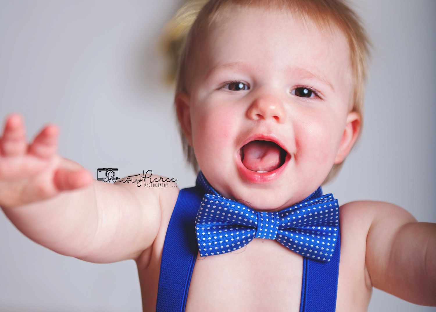 A happy baby wearing a blue polka dot bowtie and suspenders smiles brightly in a series of photos.