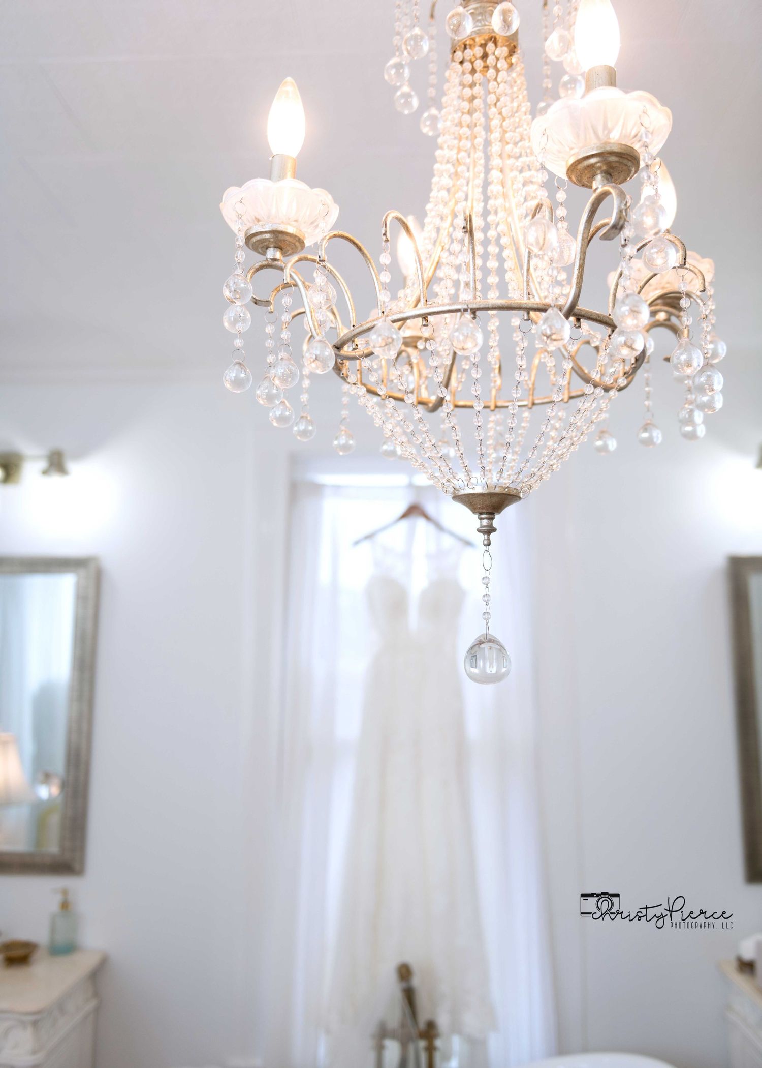 Elegant crystal chandelier illuminates a dreamy white bridal setting with soft lighting and ethereal ambiance.