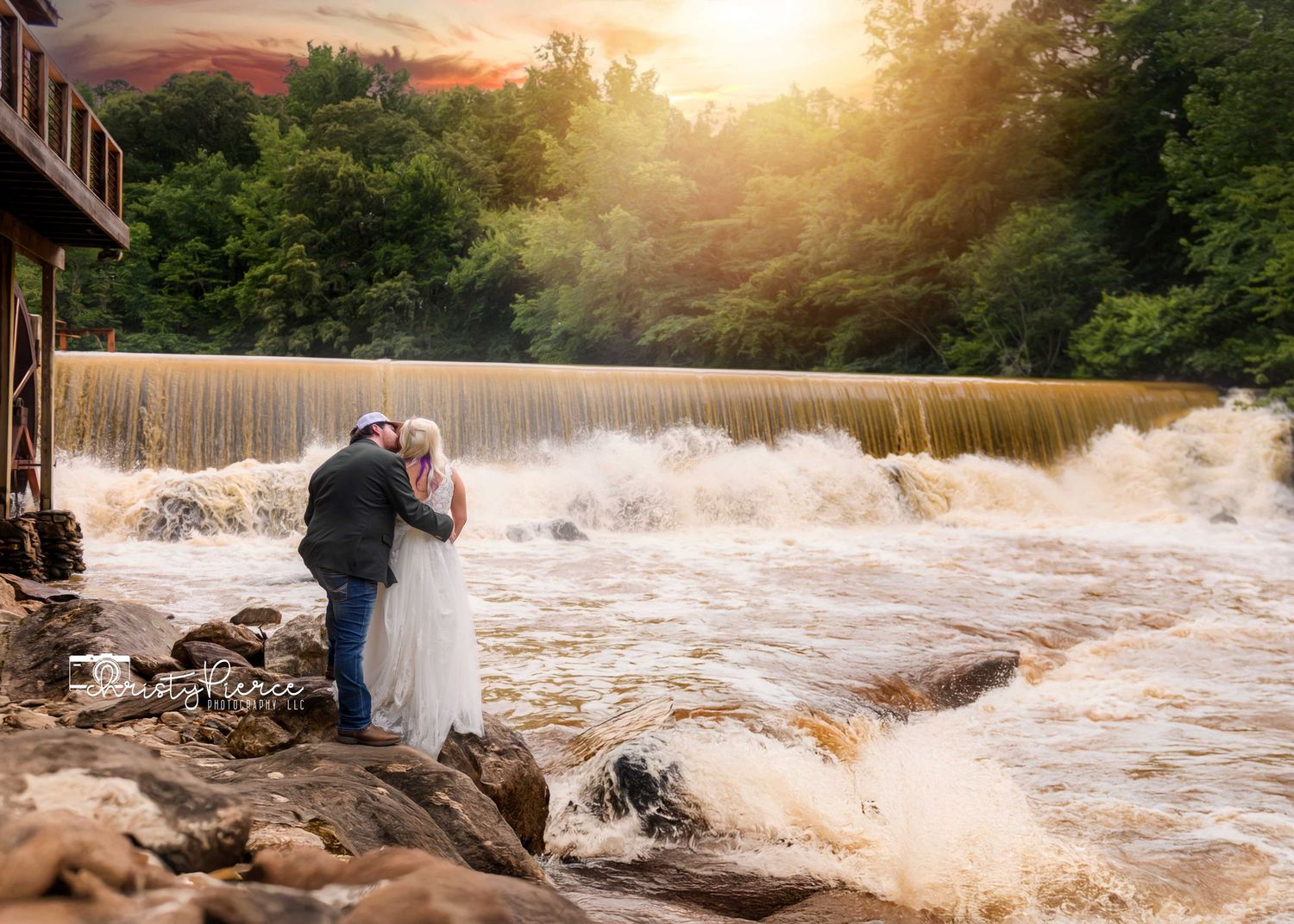 A couple stands at the edge of a rushing waterfall during golden sunset creating a romantic silhouette.