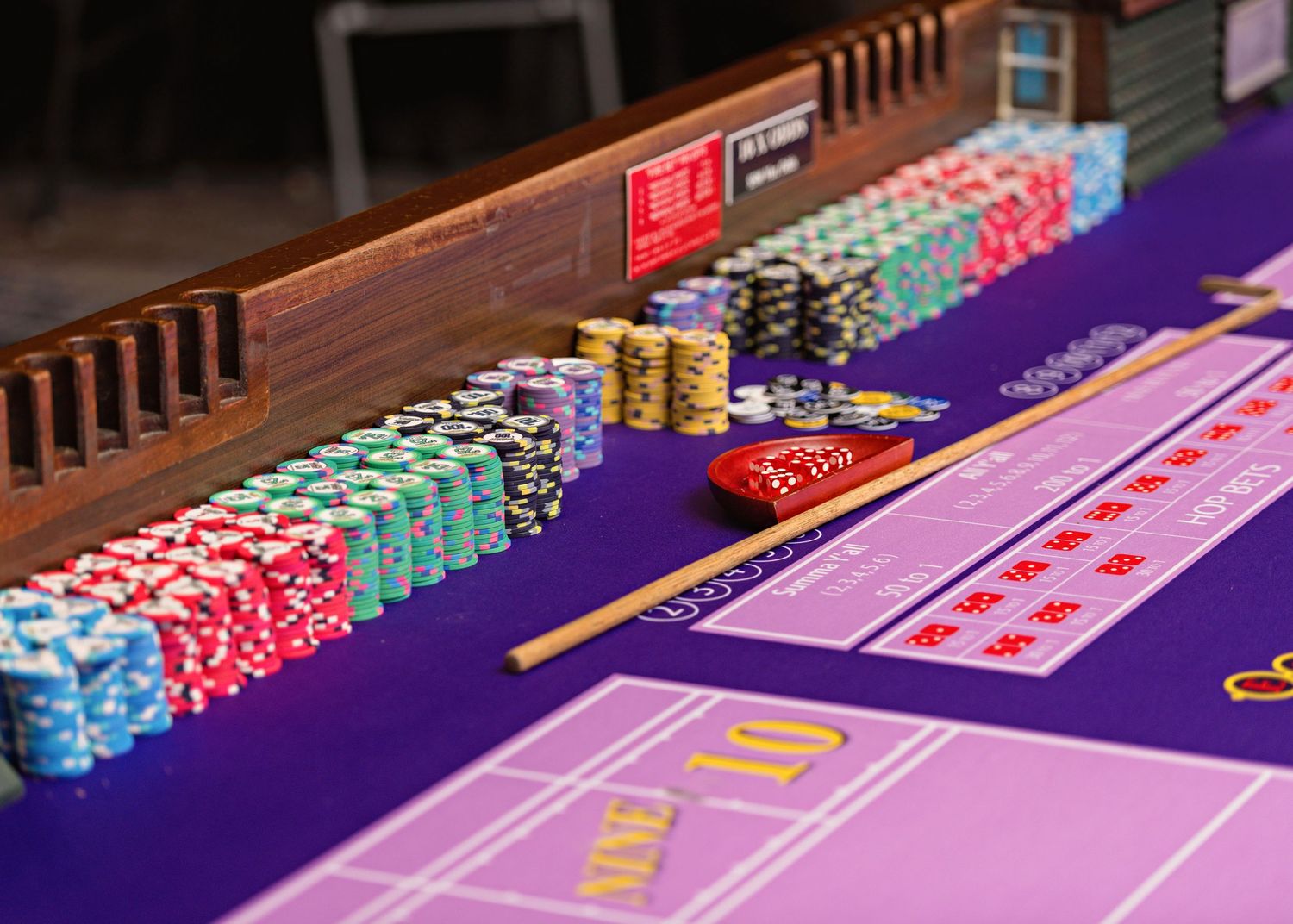 Colorful poker chips and playing cards arranged on a purple felt craps table at a casino.