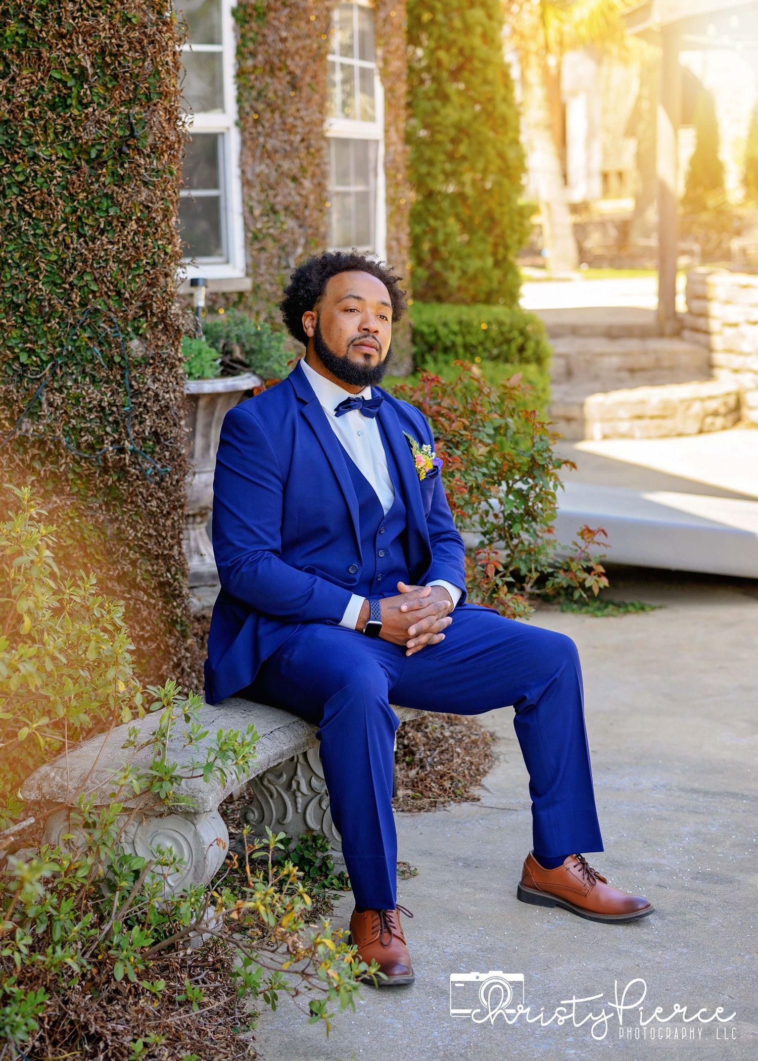 A person in a tailored royal blue suit and brown shoes poses elegantly on stone steps during a golden hour photoshoot.