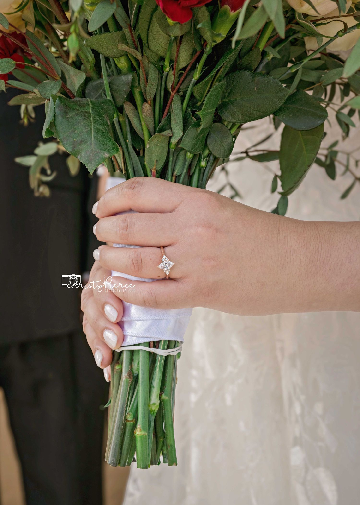 Close-up view of hands holding a bouquet of red roses wrapped in clear plastic with a white ribbon.