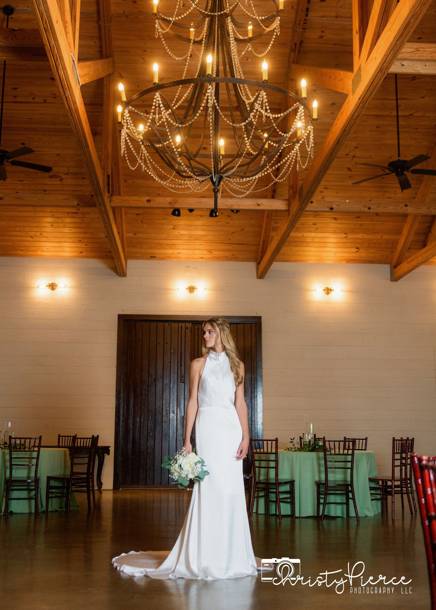 Elegant wedding venue with wooden beams, grand chandelier and mint green chairs in a rustic reception hall.