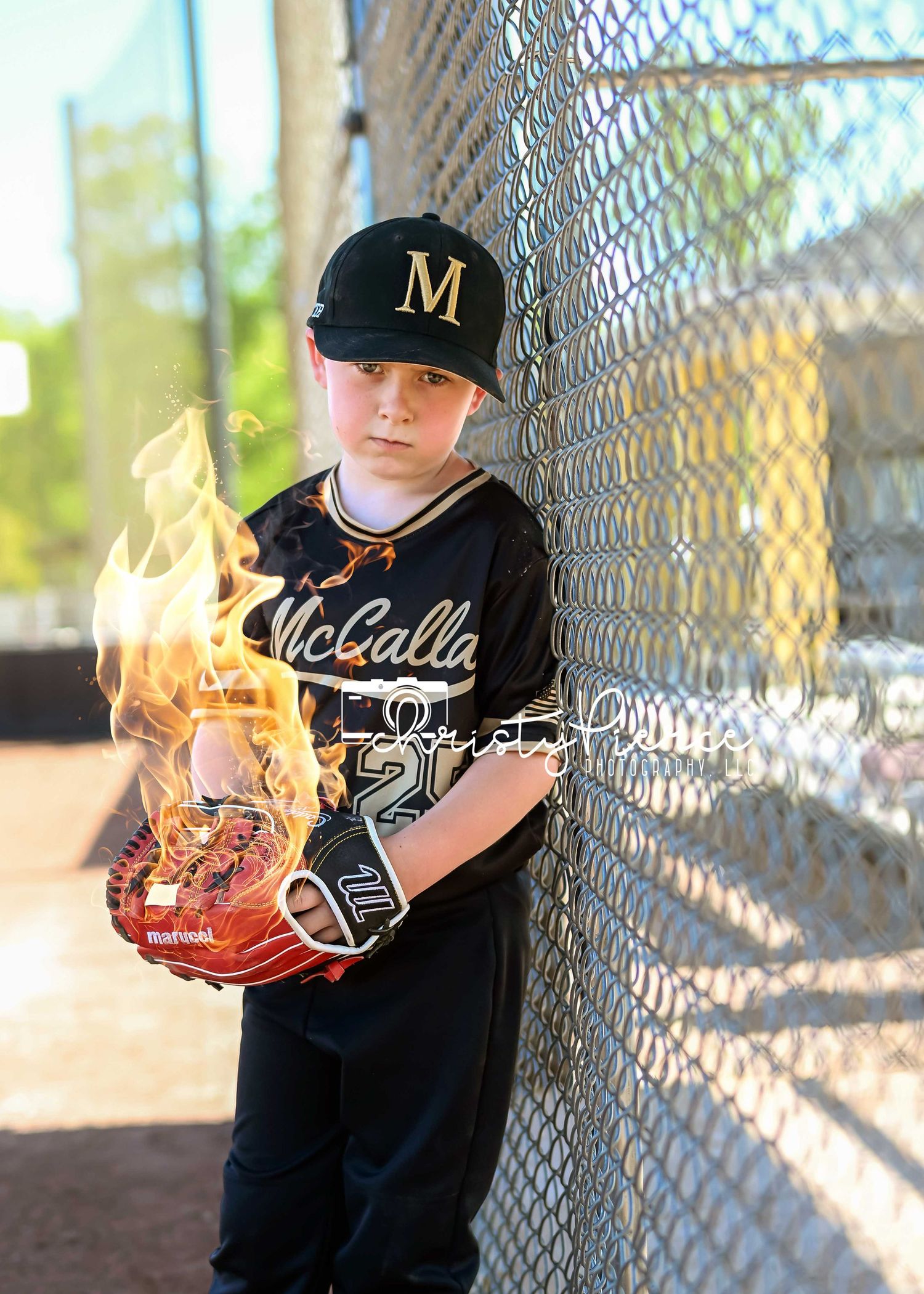 Baseball player in black uniform holds a flaming baseball glove against a chain link fence background.