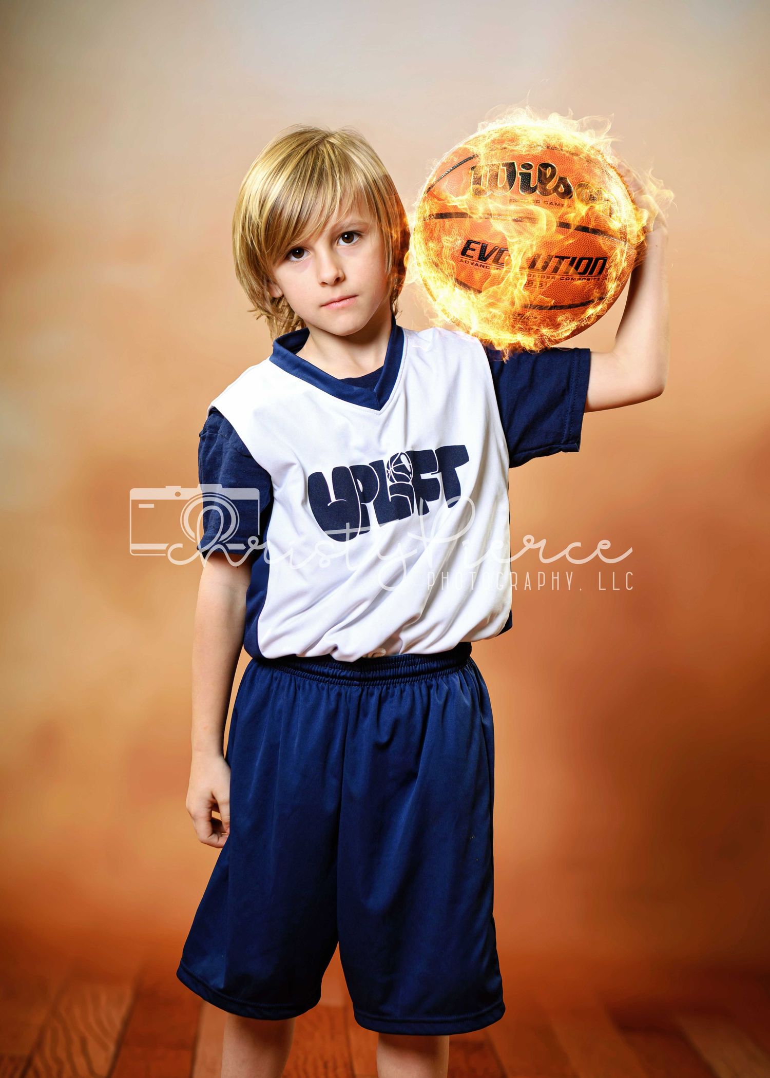 Youth basketball player in blue and white uniform holds a dramatic flaming basketball against brown backdrop.