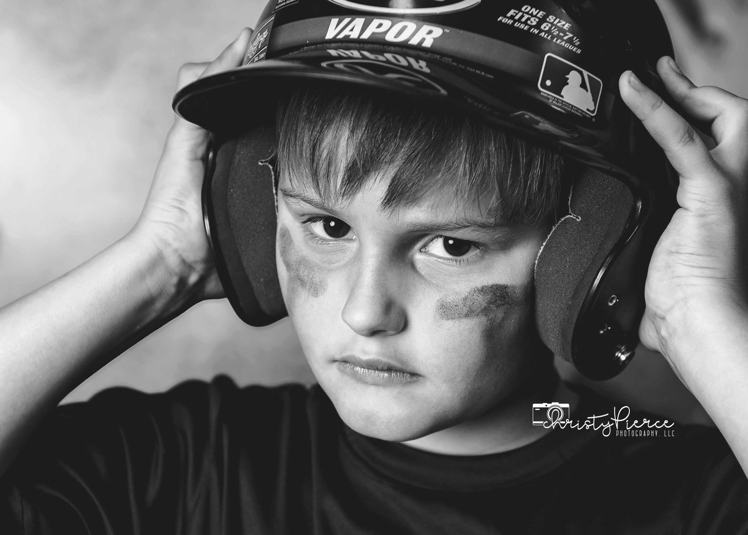 Black and white portrait of a young baseball player wearing protective headphones and a Vapor MLB cap.