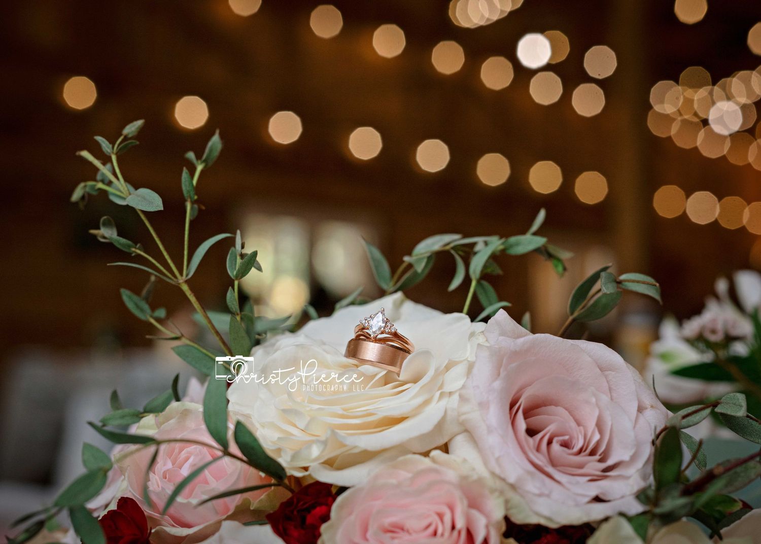 Wedding reception table decorated with blush pink roses and greenery under warm bokeh lighting.