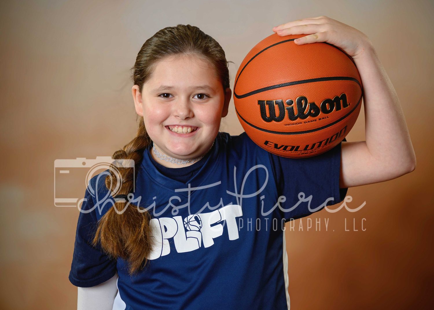 A young athlete in a navy blue JCPF t-shirt holds a Wilson basketball while posing for a sports portrait.
