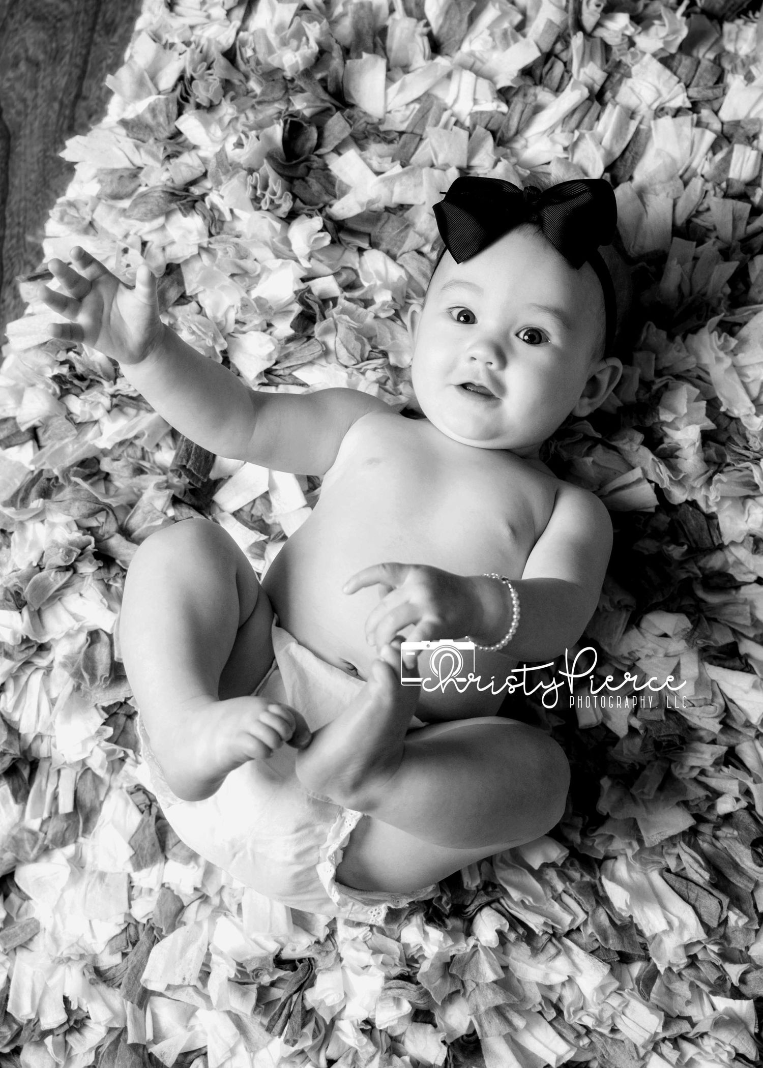 A baby lies peacefully among scattered white flower petals in a black and white artistic portrait series.