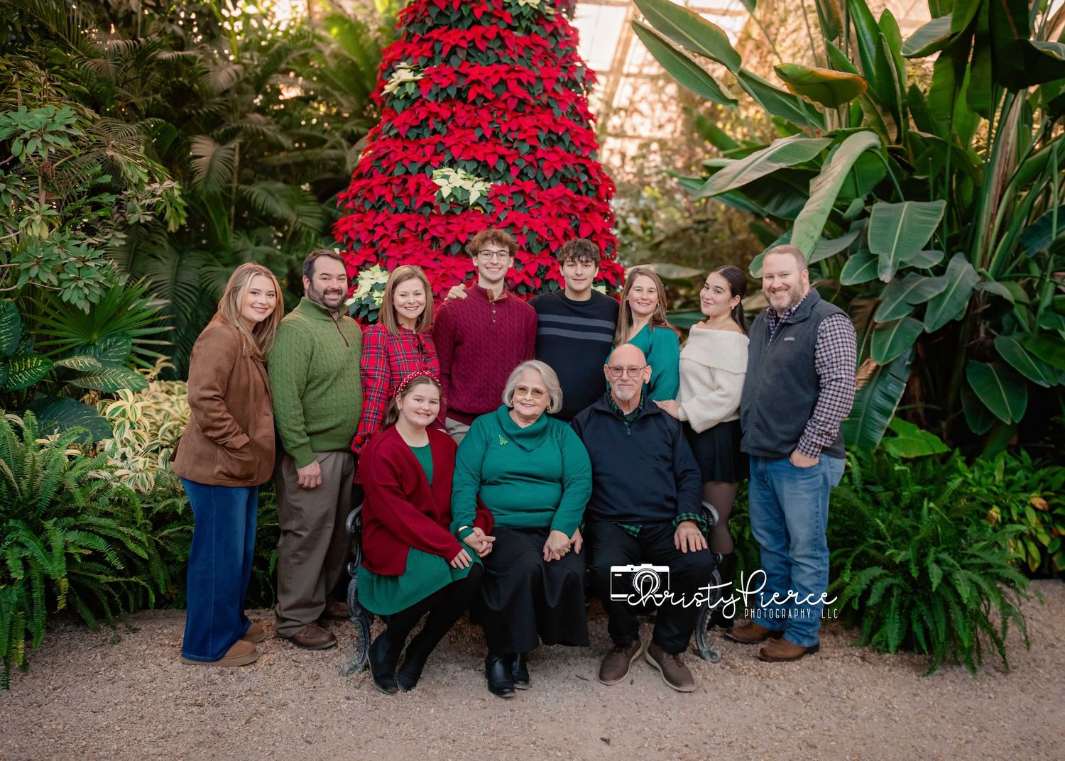 A group poses for a holiday photo in front of a towering red poinsettia tree display surrounded by lush greenery.