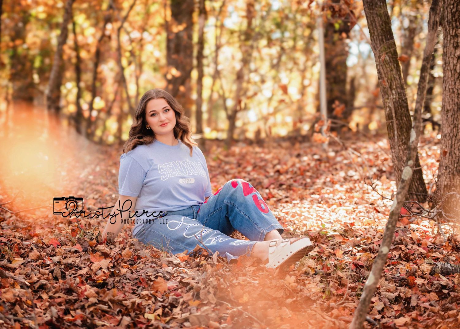 A person sits on autumn leaves in a forest with warm golden light filtering through the trees.