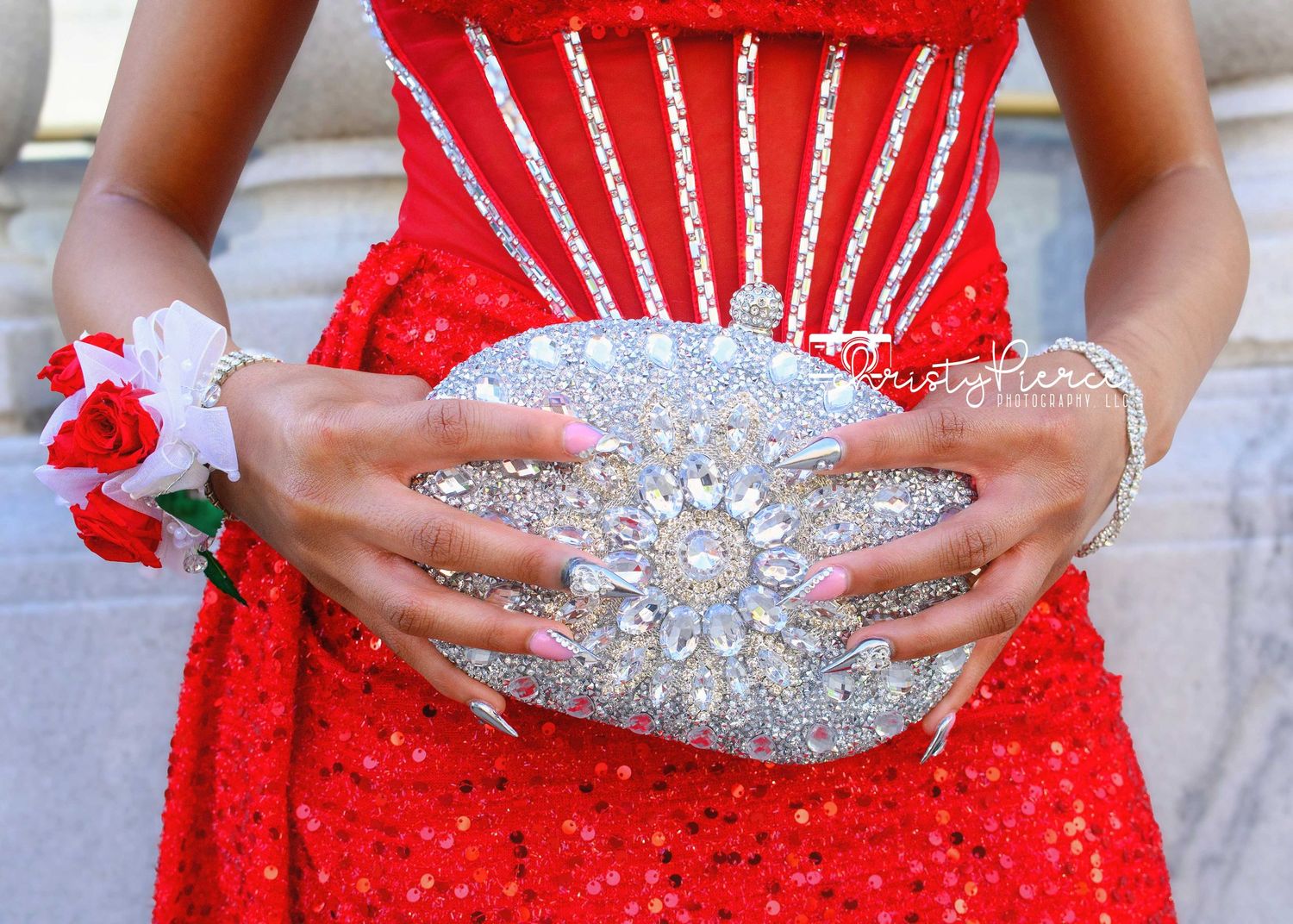 Woman in red sequin gown holding sparkling crystal rhinestone oval clutch purse with floral wrist corsage.