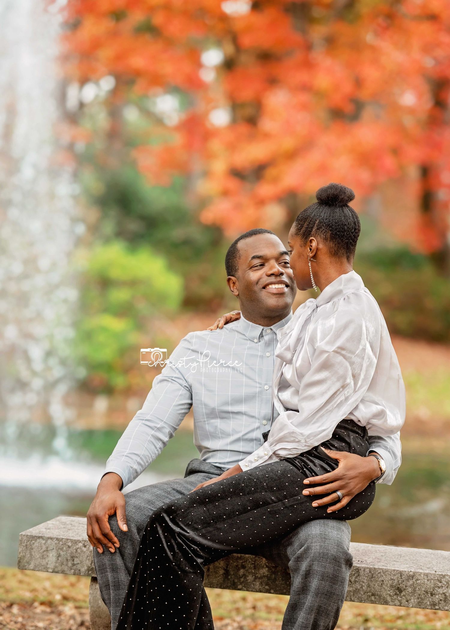Couple sharing a romantic moment by a fountain with vibrant autumn foliage in the background.