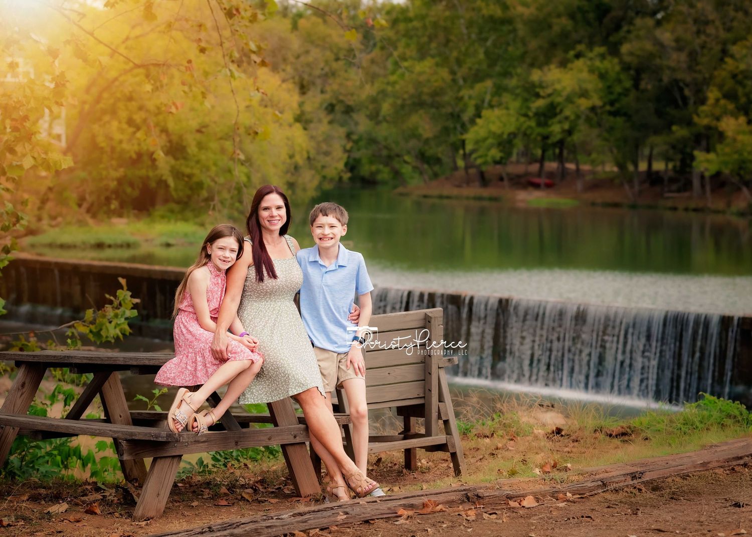 People sitting on a wooden bench by a serene lake with a waterfall in the background during autumn.