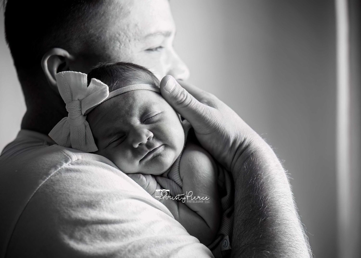 A peaceful black and white portrait of a sleeping newborn baby resting on someone's shoulder.