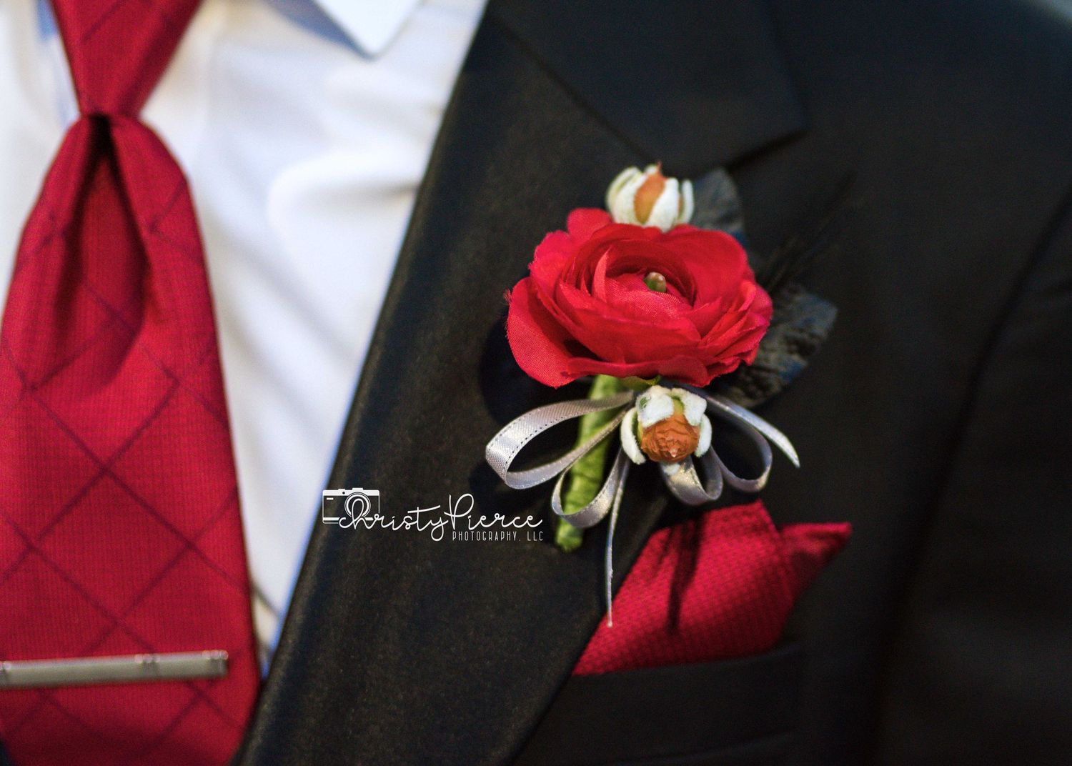 Close-up of red rose boutonniere pinned to black suit lapel with white dress shirt and red tie.