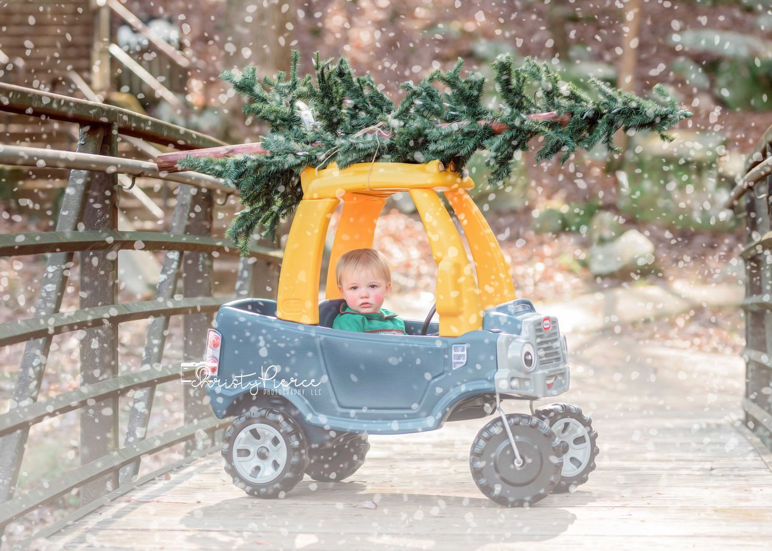 A toy Cozy Coupe car sits in falling snow with evergreen branches visible in the background.