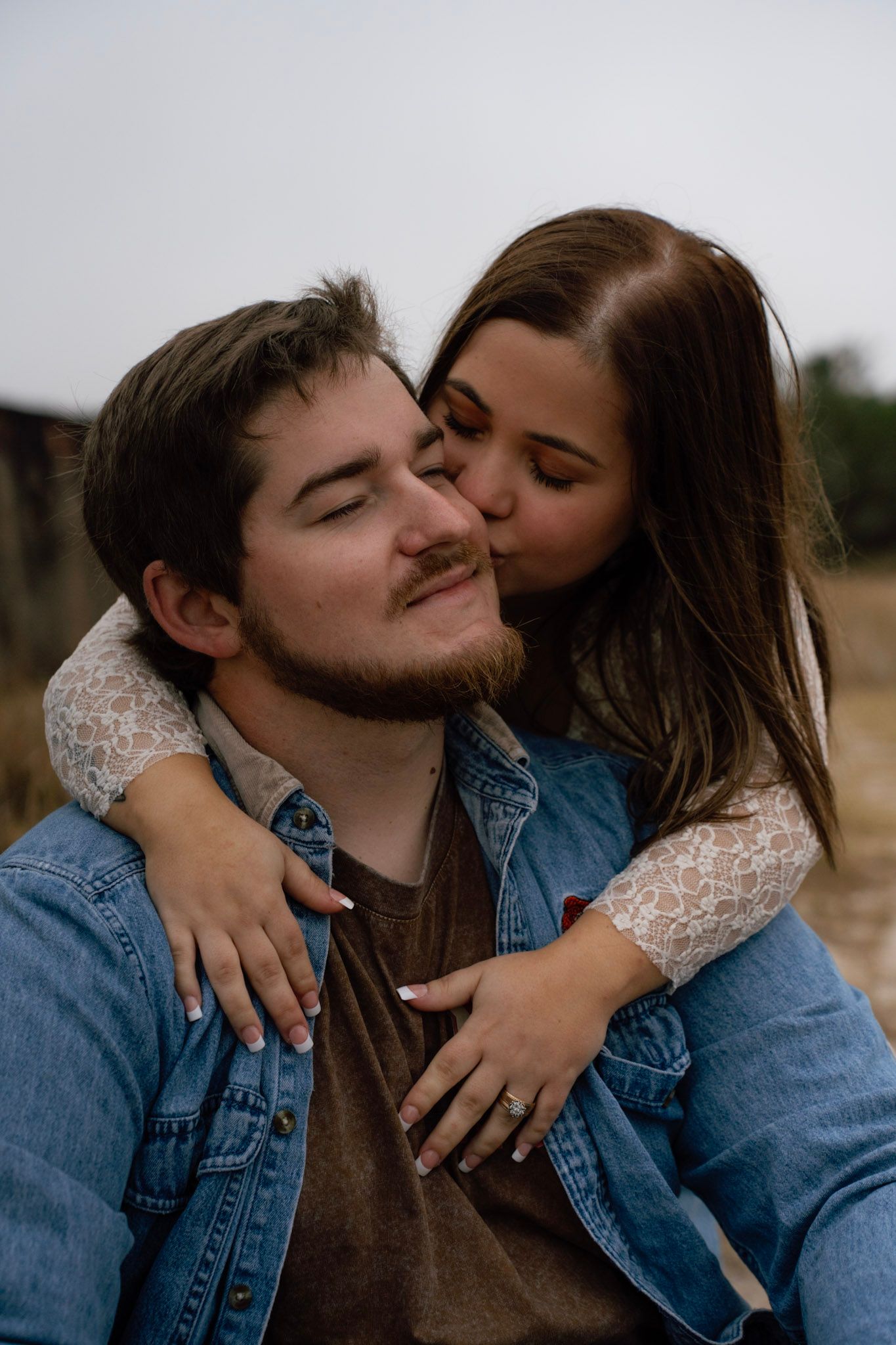 A romantic couple embraces outdoors wearing denim and lace while sharing tender moments in a field.