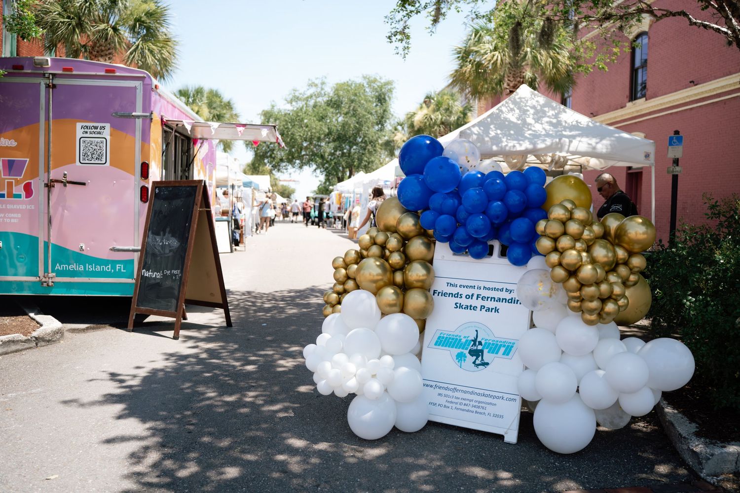 Colorful balloon arch display at an outdoor Friends of Fernandina Book Fair event with white tents and vendors.