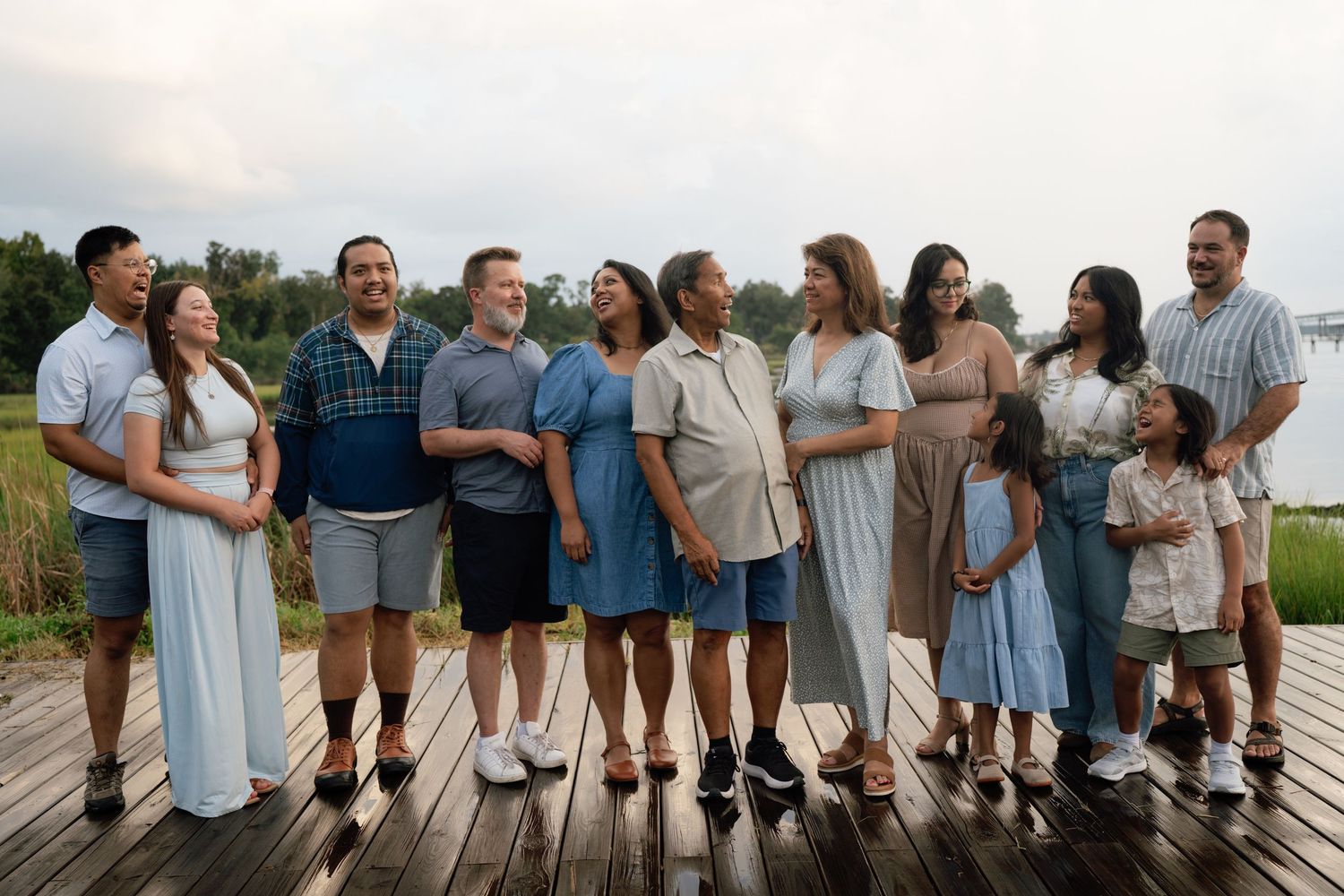 Large multigenerational family group smiling together on a wooden dock surrounded by lush greenery.