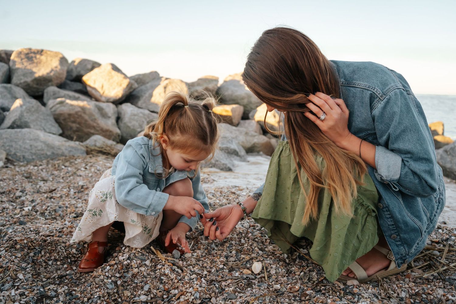 A parent and child explore rocks together on a rocky beach at sunset.