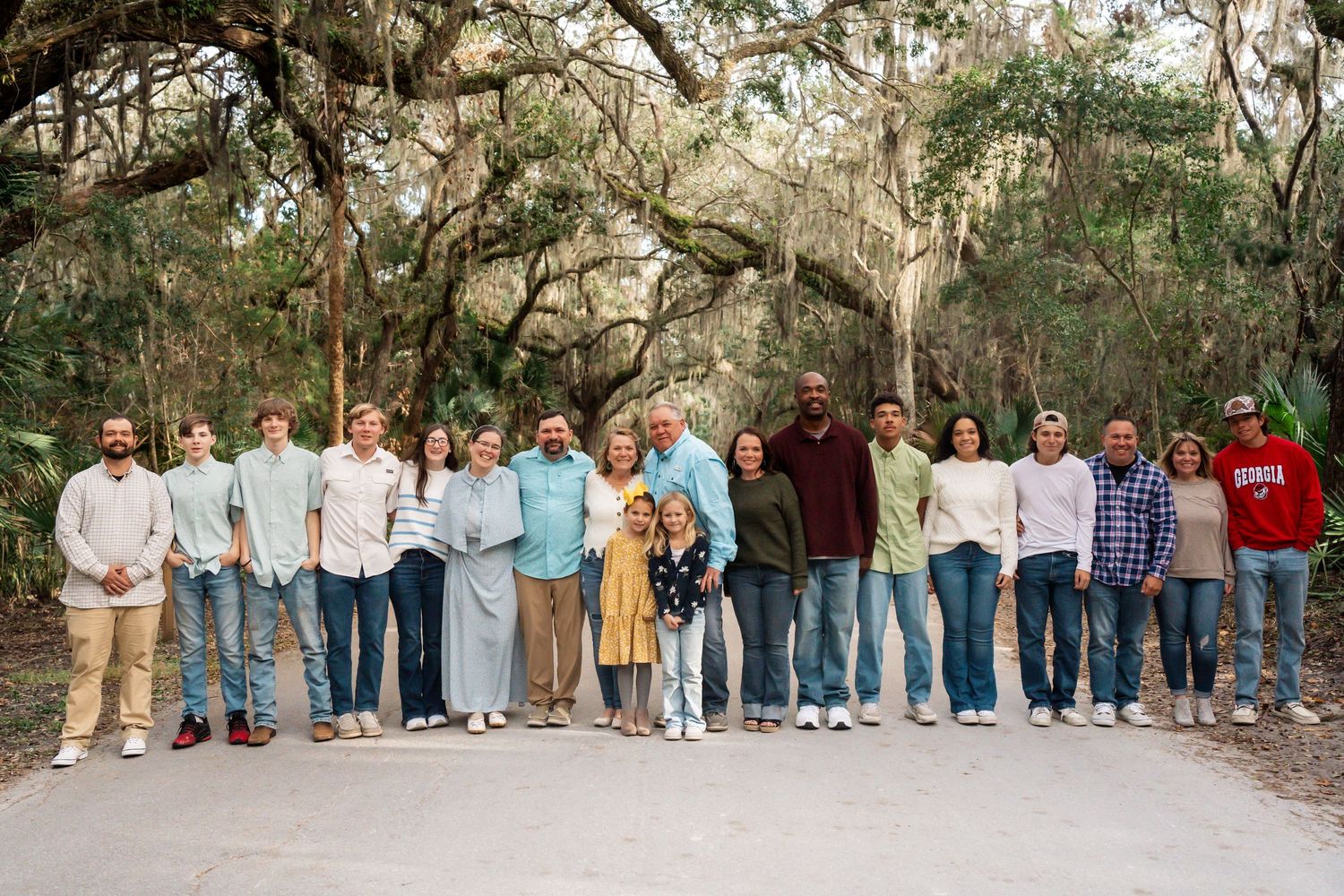Large group photo of people standing together under moss-covered oak trees.