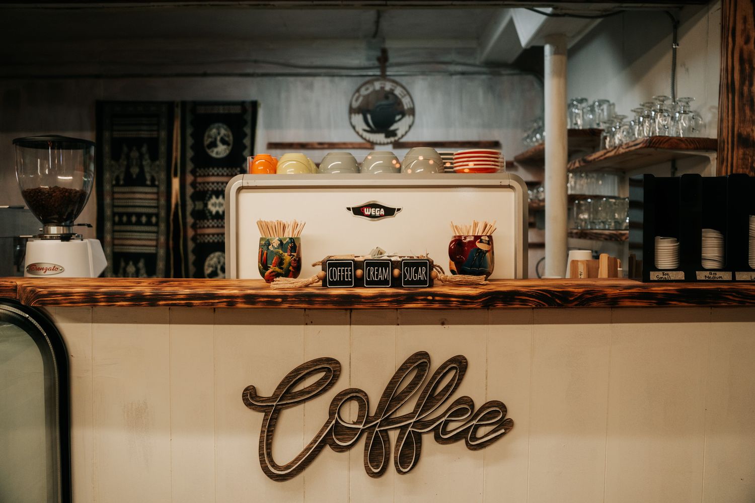 Vintage coffee shop counter with wooden shelves and retro coffee sign display against cream colored wall.
