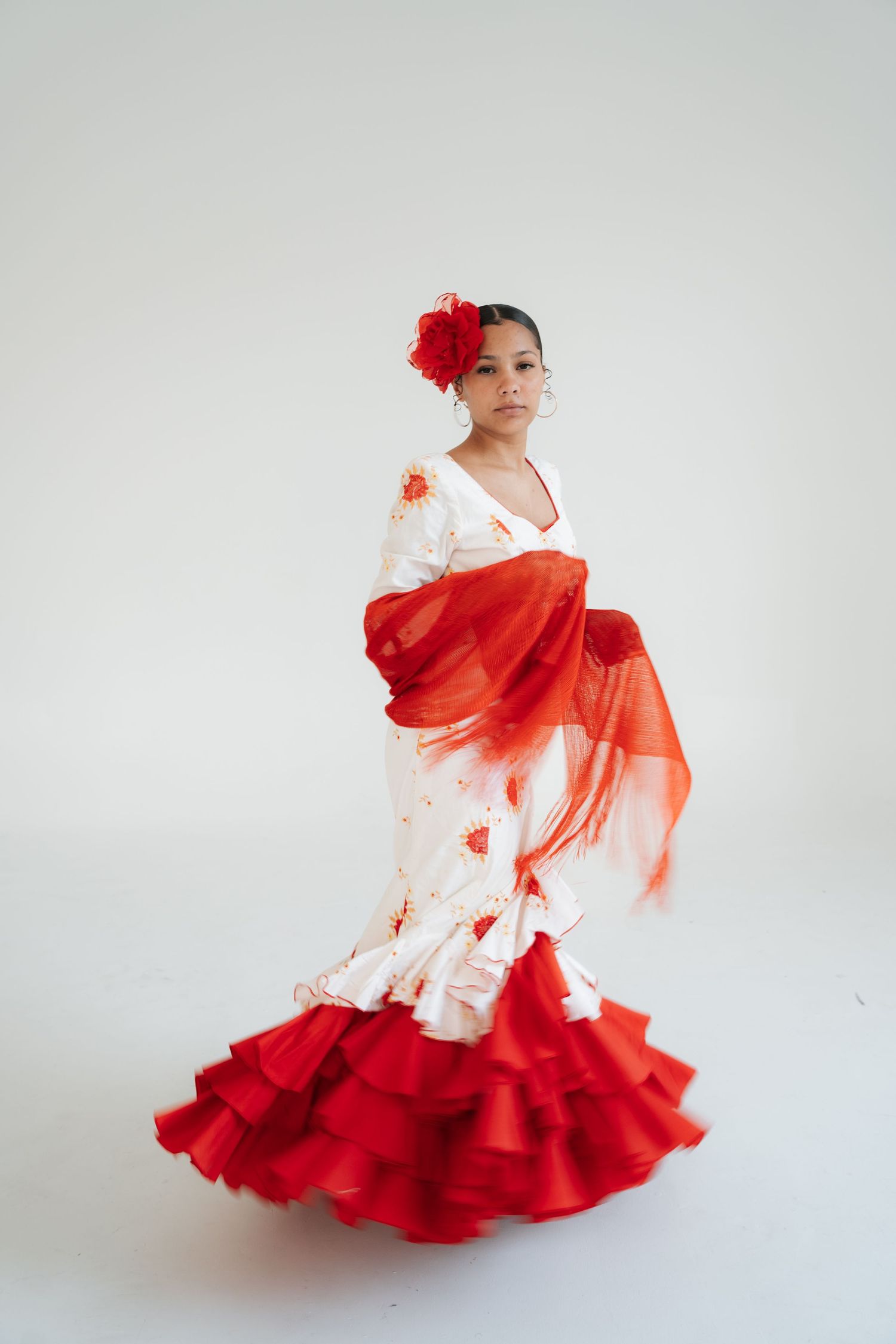 Elegant flamenco dancer in white dress with red ruffles and flower poses gracefully against white background.