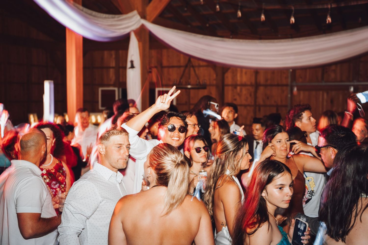 Crowded indoor party with guests dancing and celebrating in a rustic barn venue with warm lighting.